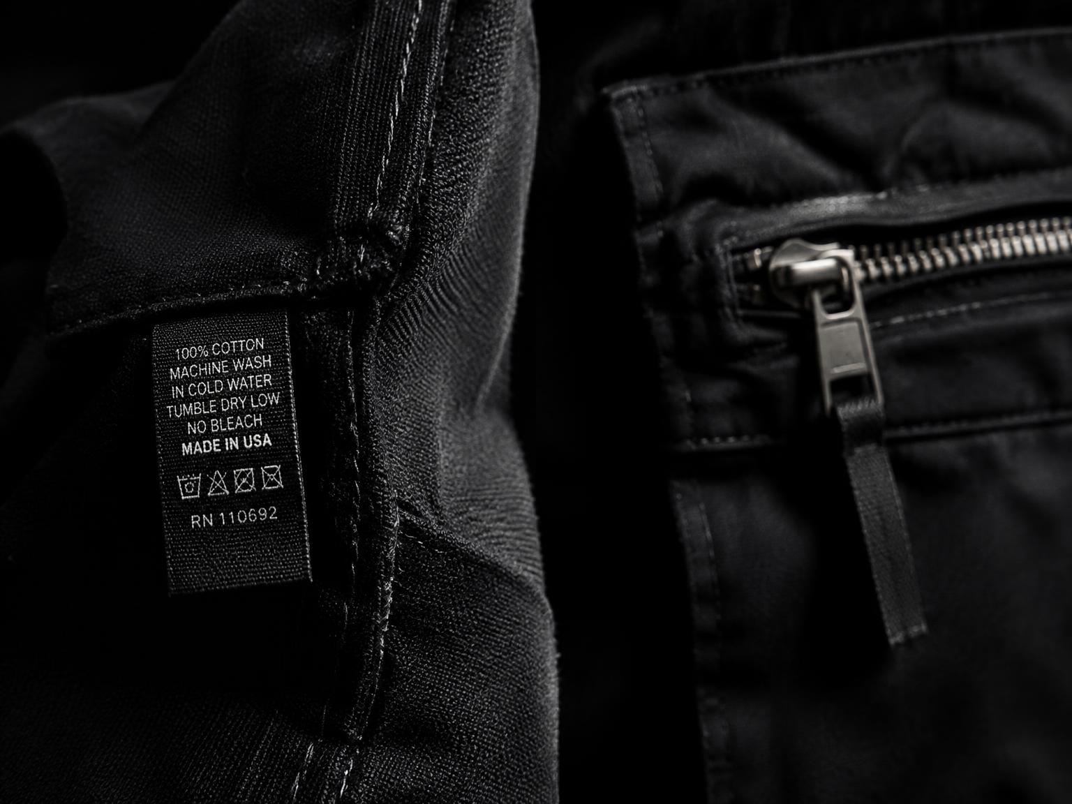 Close-up of a black garment seam, woven label, and zipper detail